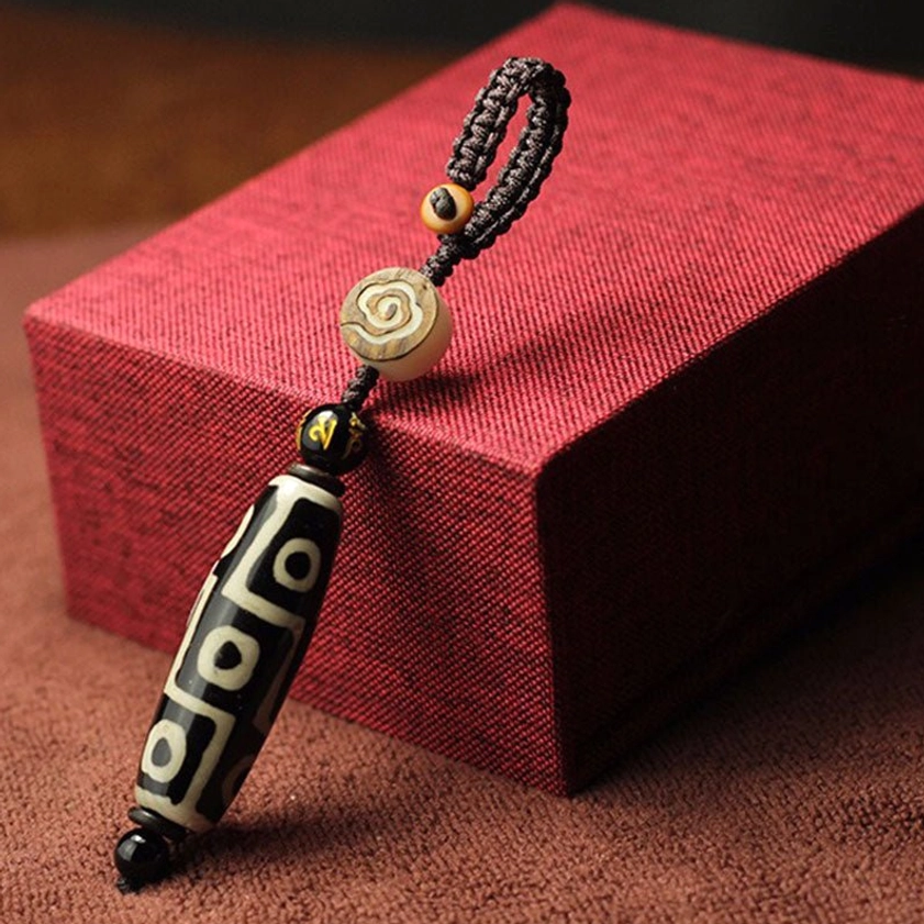 Black and white striped dzi bead keychain with geometric square motifs and wooden accent bead on red gift box for Buddhist protection amulet