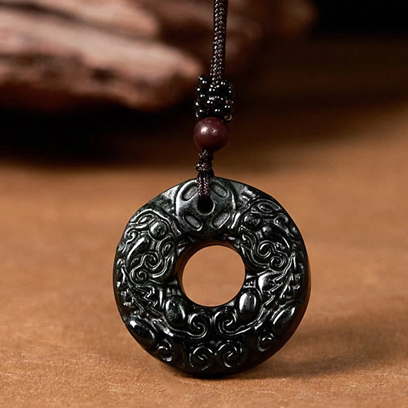 Buddhist jade peace buckle necklace with Pixiu motif and dark braided strap against wooden surface