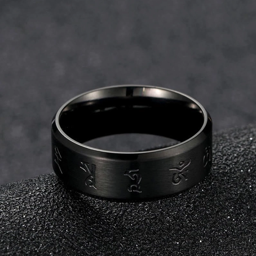 Flat lay top-down shot of black Jambhala titanium steel ring showing clearly engraved mantras and brushed exterior with polished inner surface