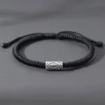 Black koi fish bracelet overhead flat lay showing adjustable sliding knot and silver fish charm on grey background