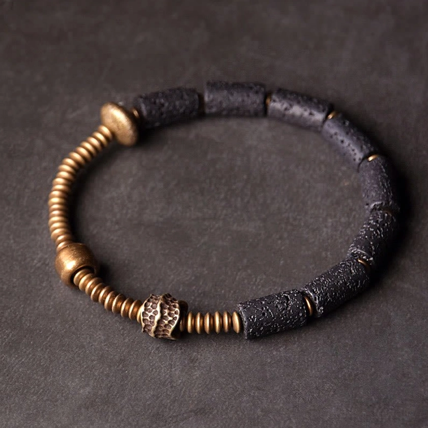 Black lava rock and copper beaded bracelet top-down flat lay showing cylindrical lava beads with hammered copper accent