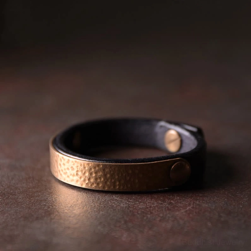 Black leather and copper brass bangle bracelet featuring textured metal panel and secure buckle closure