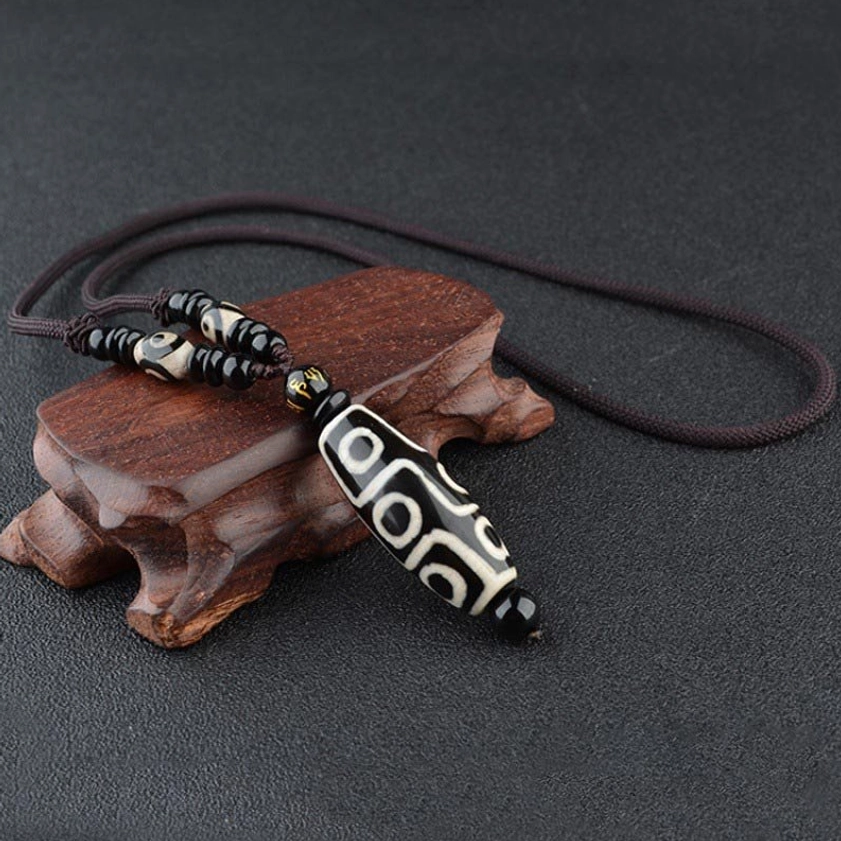 Black nine-eye dzi bead Buddhist necklace pendant displayed on wooden stand showing intricate hand-painted eye details