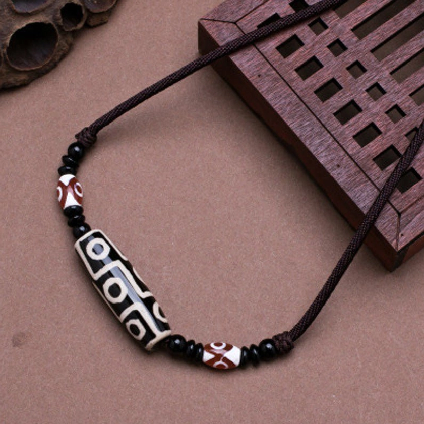 Black nine-eye dzi bead Buddhist necklace with braided cord and small agate spacer beads, overhead flat lay view on wooden background
