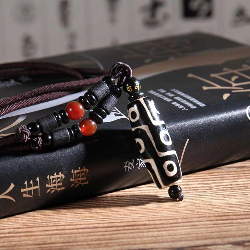 Black-white nine-eye dzi bead necklace with brown cord and red agate accents displayed close-up