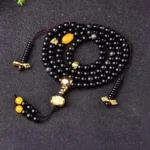 Black obsidian 108 bead mala bracelet with gold-tone hardware and amber accents displayed on dark background