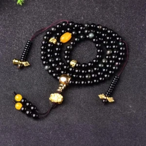Black obsidian 108 bead mala bracelet with gold-tone hardware and amber accents displayed on dark background