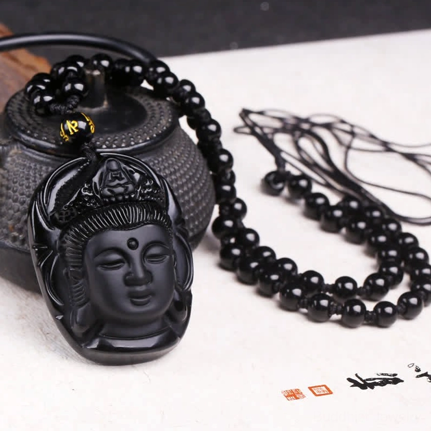 Black obsidian Avalokitesvara Kwan Yin pendant necklace with gold mantra bead displayed on desktop with cast iron teapot, top-down view