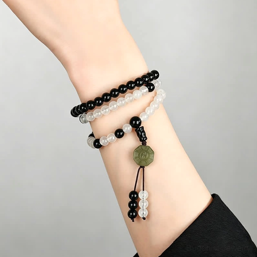 Layered Black Obsidian protection bracelets stacked on wrist with green jade Bagua charms and tassels