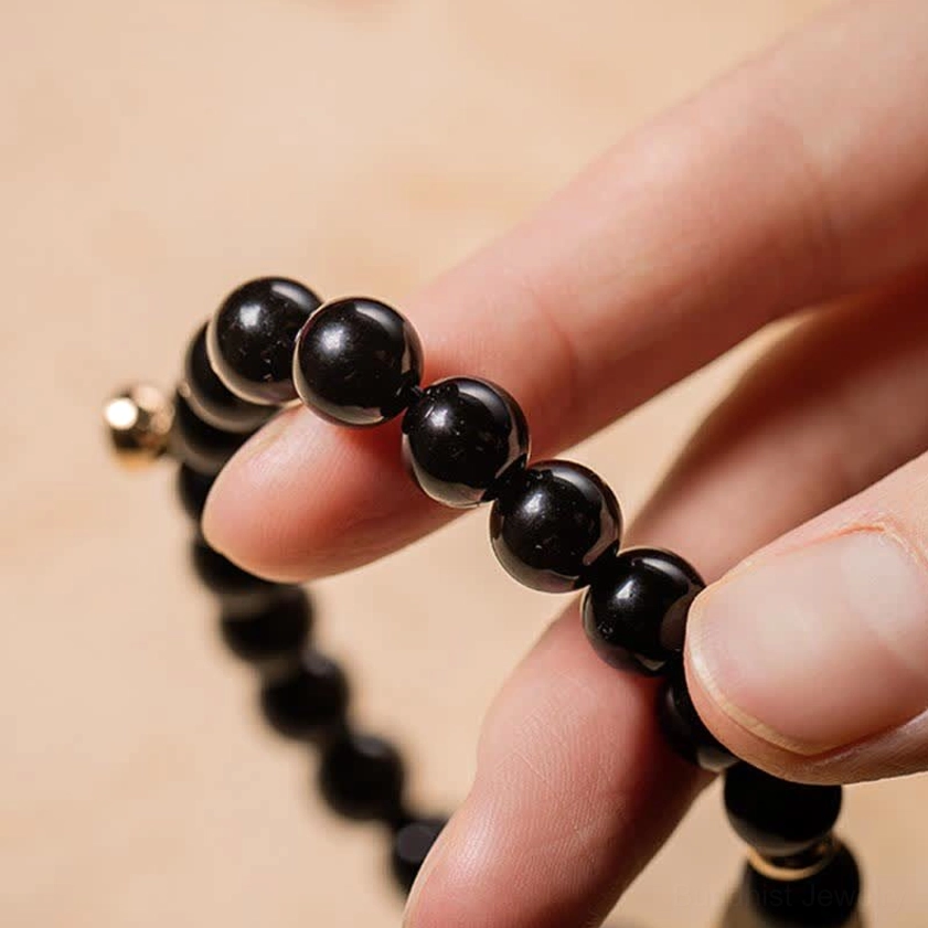 Extreme close-up of high-gloss black obsidian beads held between fingers, showing polished surface and gold-toned metal accent details