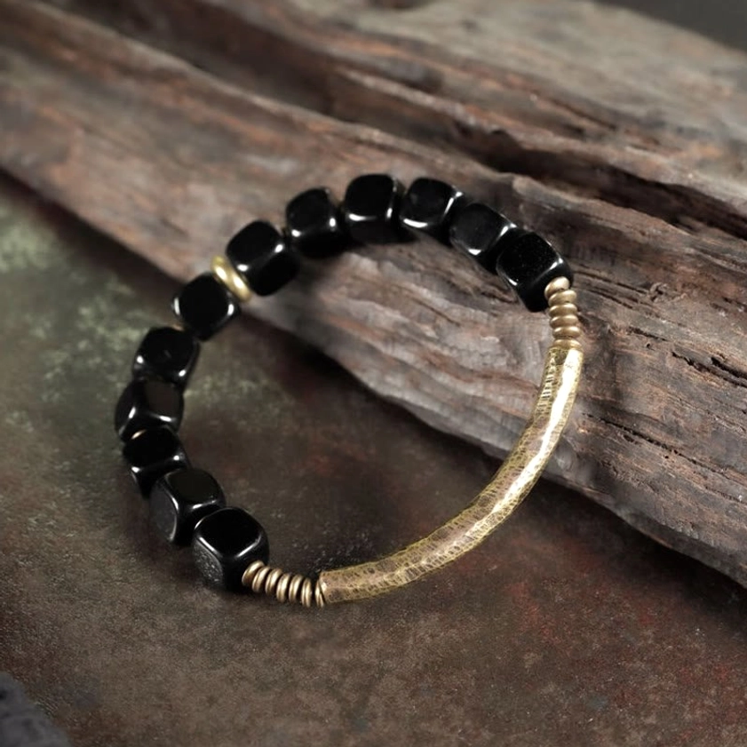 Black cube obsidian beads with hammered gold metal ring on premium elastic cord wooden background