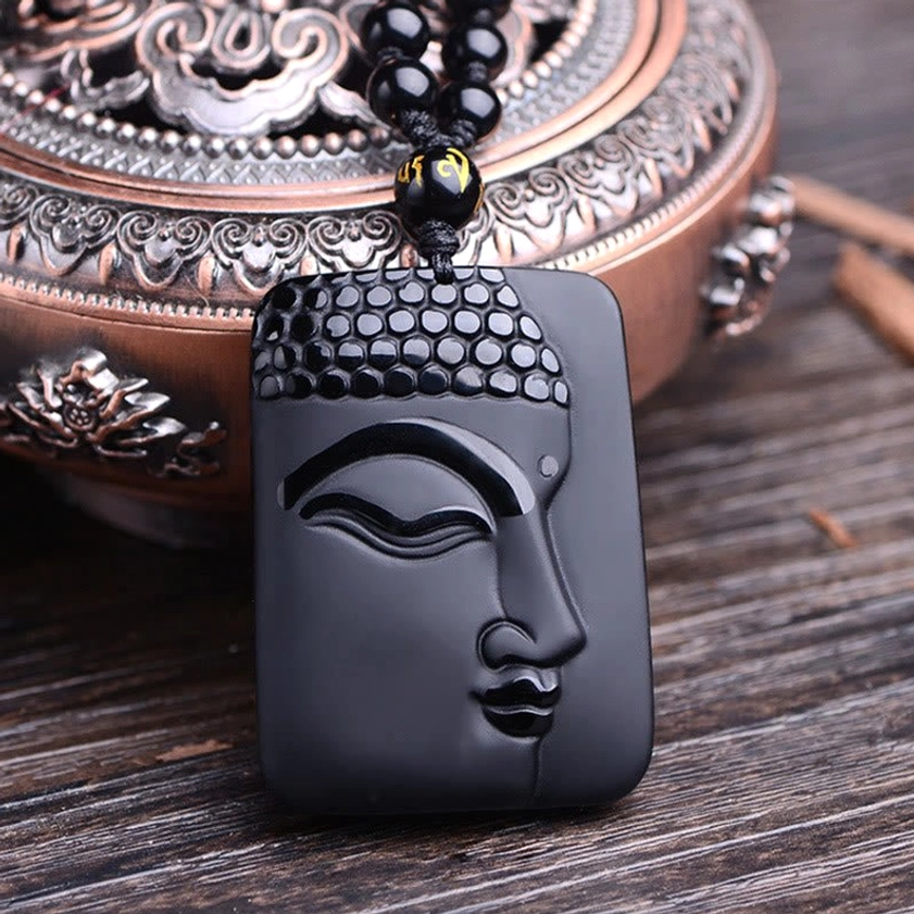 Black Obsidian Buddhist Pendant - Front-facing close-up of polished obsidian pendant with intricate Buddha facial carving and branded spacer bead