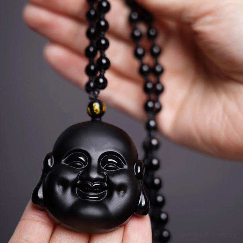 Black obsidian laughing Buddha pendant held in hand, showing carved smiling Buddha face detail