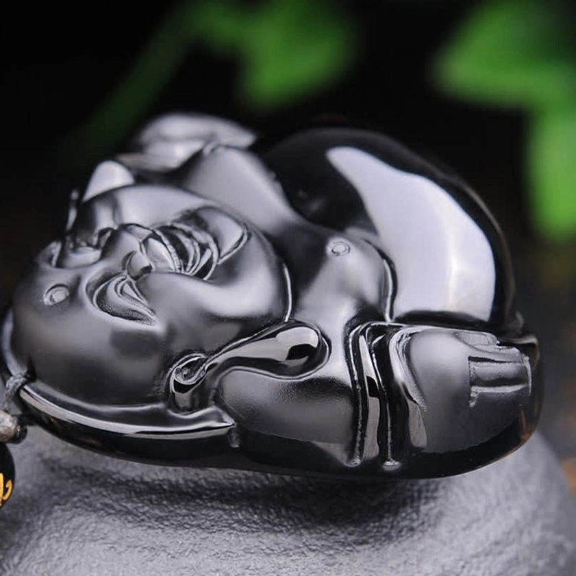 Side profile view of Black Obsidian Laughing Buddha pendant lying flat, showing curved back profile and stone texture