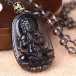 Black obsidian carved Buddha pendant necklace with beaded chain, left-top angled view on linen fabric and wooden tray
