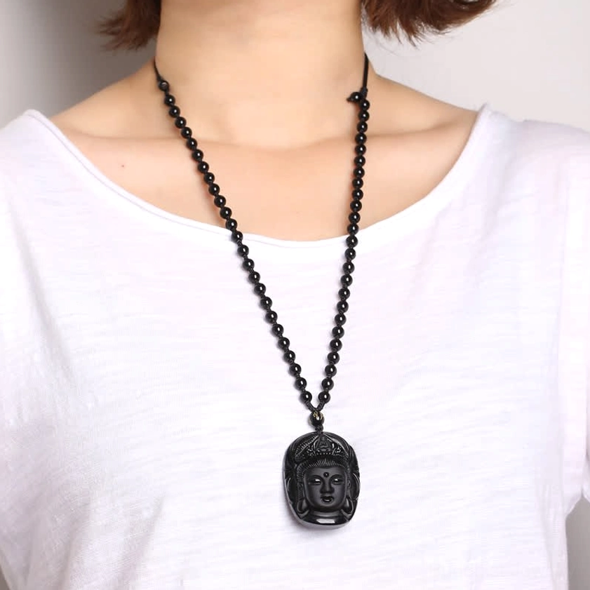 Black obsidian Avalokitesvara Buddha head pendant with polished matte surface and six-word mantra spacer bead, front oblique view with cast iron teapot