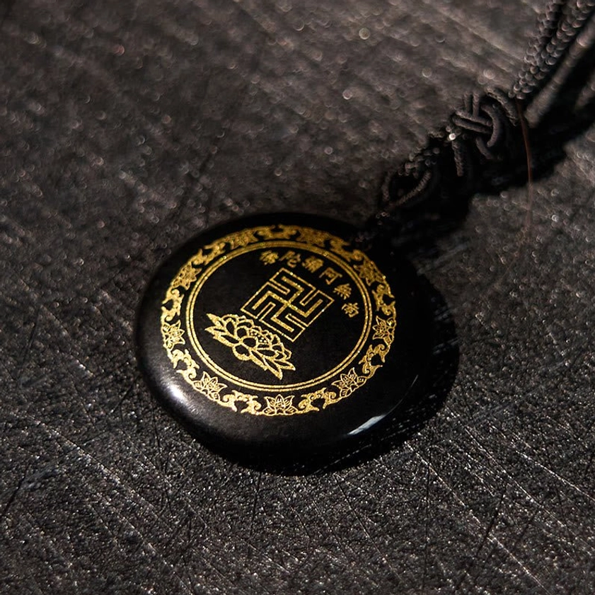 Handcrafted black obsidian Buddhist pendant overhead flat lay showing swastika lotus gold pattern detail