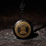 Black obsidian Buddhist pendant with gilded swastika and lotus symbol, front close-up view on leather background