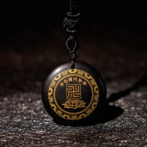 Black obsidian Buddhist pendant with gilded swastika and lotus symbol, front close-up view on leather background
