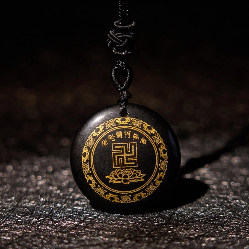 Black obsidian Buddhist pendant with gilded swastika and lotus symbol, front close-up view on leather background