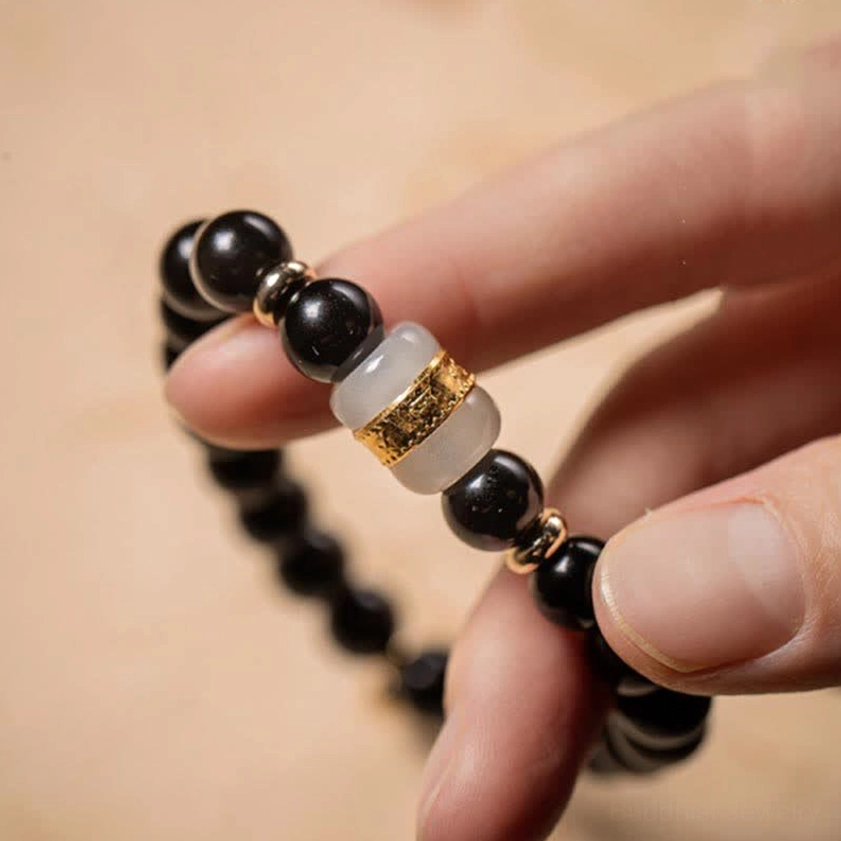 Close-up of black obsidian and jade Buddhist bracelet held in hand, showing polished black beads with distinct gold-plated and jade accents