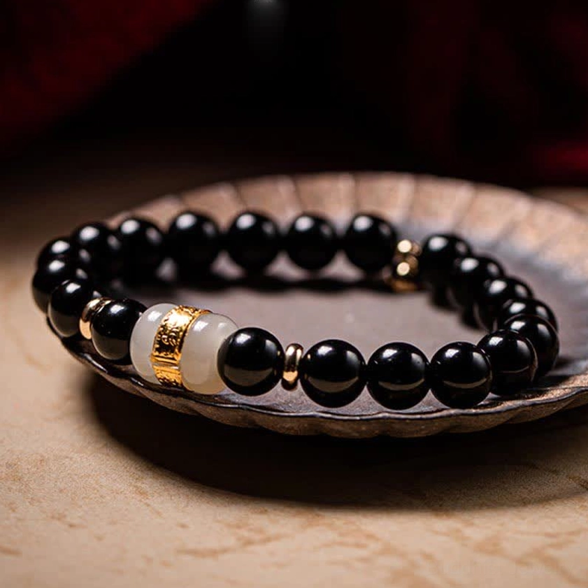Black Obsidian and Jade Om Mani Padme Hum couples bracelet displayed on vintage ceramic tray, showing smooth round black beads with light jade and gold-plated spacers