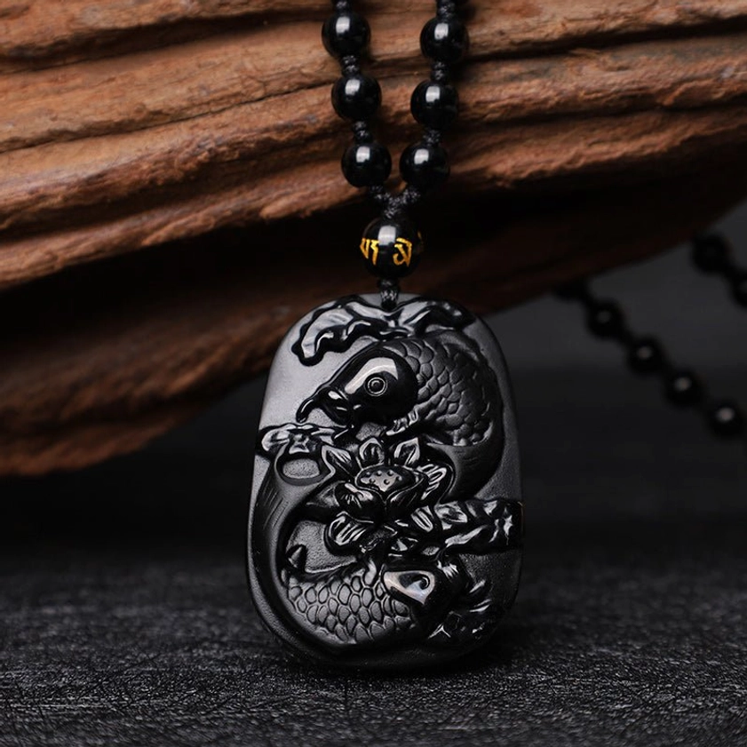 Handcrafted Black Obsidian Koi Fish Lotus Pendant - three-quarter front view on wooden surface displaying carved motifs
