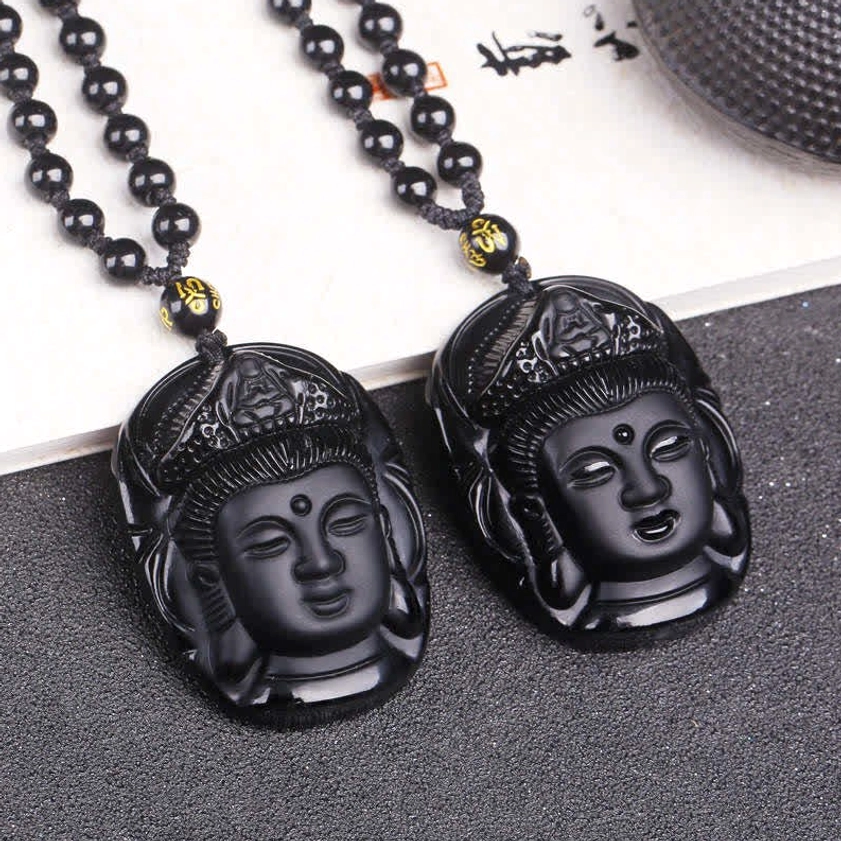 Two identical black obsidian Avalokitesvara Buddhist pendants with beaded chain and gold spacer beads on grey textured background