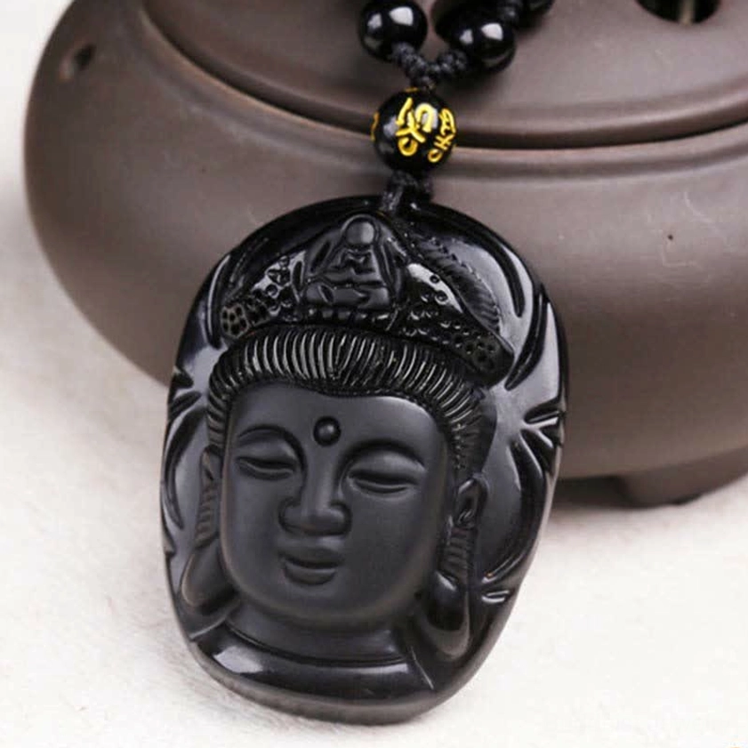 Black obsidian Avalokitesvara pendant flat lay showing sacred crown carving and mantra spacer bead detail with dark pottery background