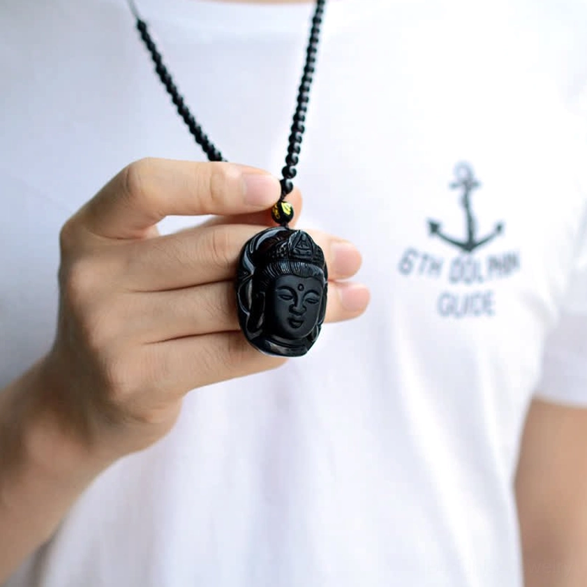 Hand-held close-up of black obsidian Avalokitesvara pendant showing intricate carved facial details and smooth matte finish