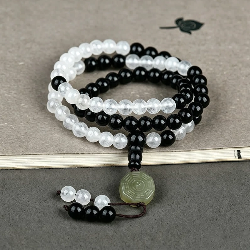 Stacked Black Obsidian and white crystal bracelets with layered Bagua jade charms on book display