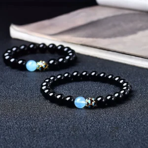 Black obsidian lotus bracelet with light blue accent bead and engraved metal spacer, displayed on hardcover book