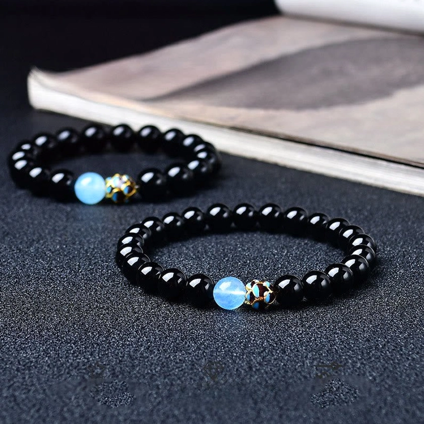 Black obsidian lotus bracelet with light blue accent bead and engraved metal spacer, displayed on hardcover book