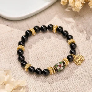 Black obsidian lotus protection bracelet with gold cloisonné enamel charm flat lay