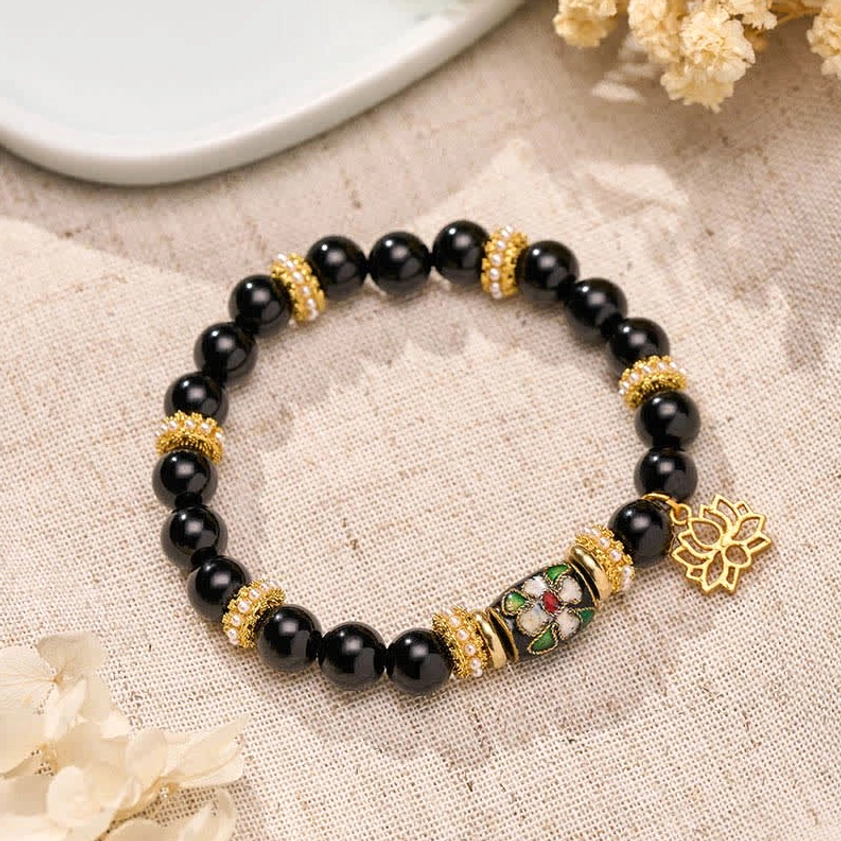 Black obsidian lotus protection bracelet with gold cloisonné enamel charm flat lay