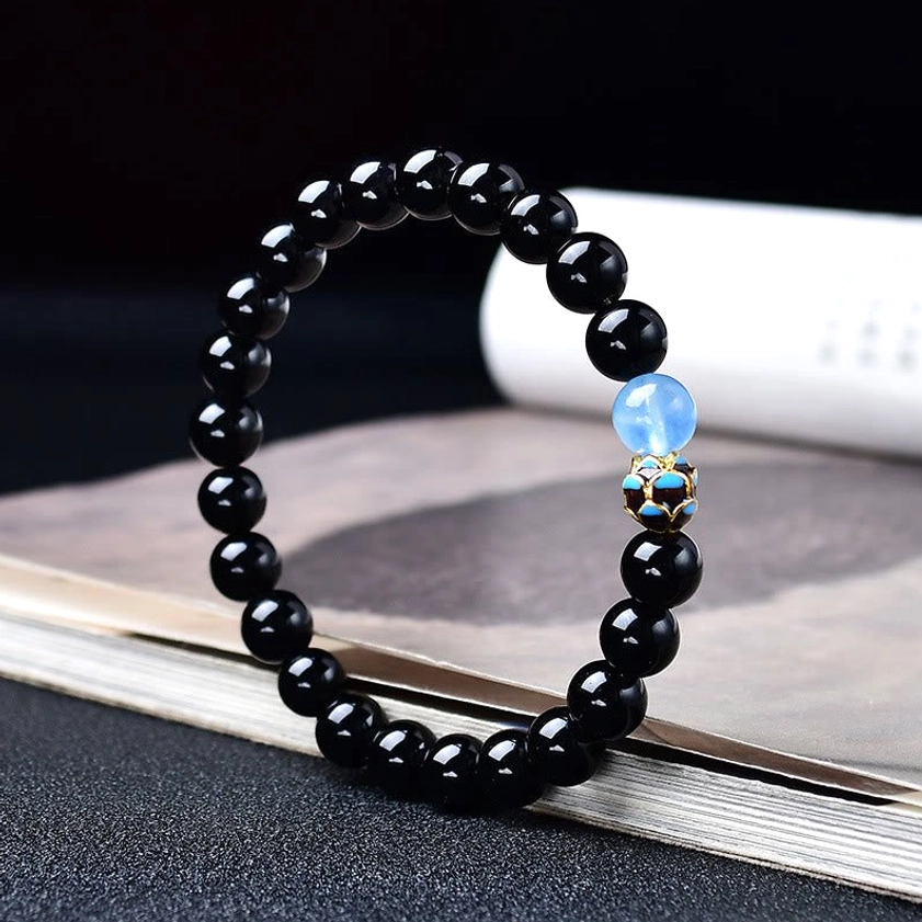 Black obsidian lotus bracelet with light blue accent bead on book, showing bead quality and craftsmanship