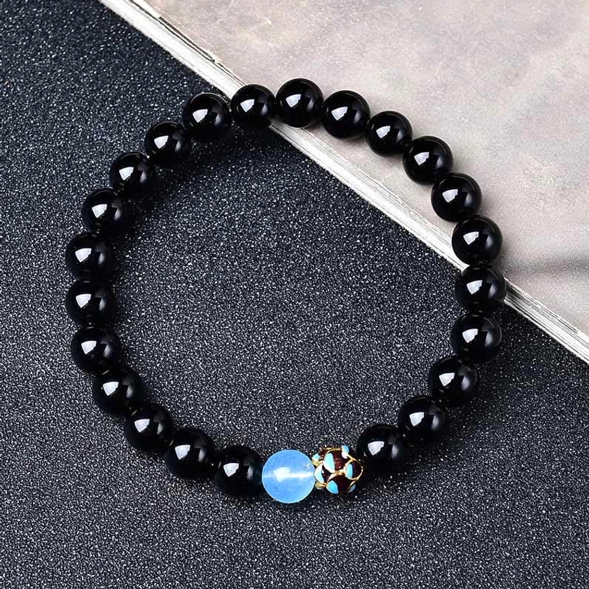 Single black obsidian lotus bracelet flat lay showing polished beads, decorative blue bead, and metal engraving details