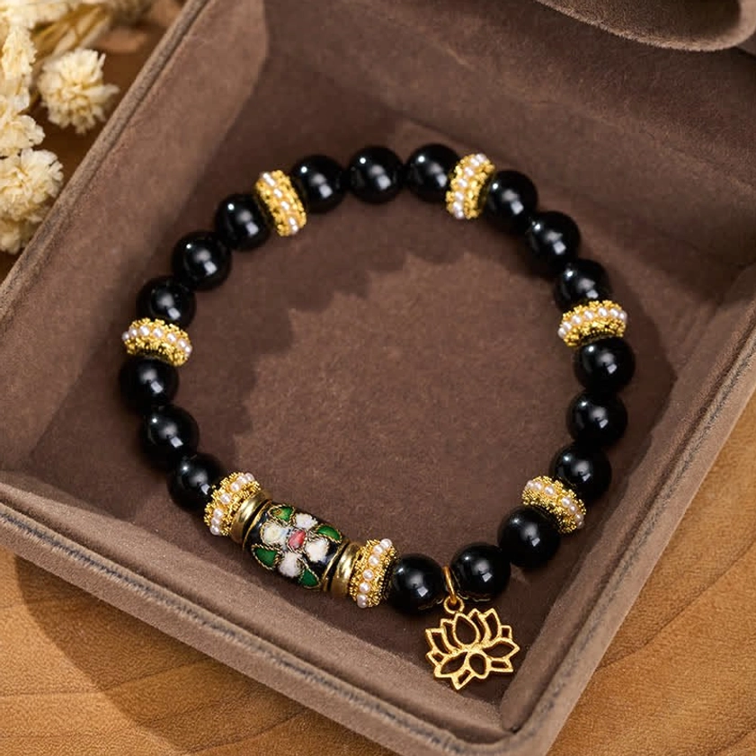 Black obsidian beaded bracelet with gold lotus pendant displayed in velvet jewelry box