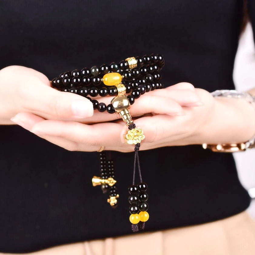 Close-up of black obsidian mala bracelet held in hands showing polished beads, gold decorative accessories and tassel pendant