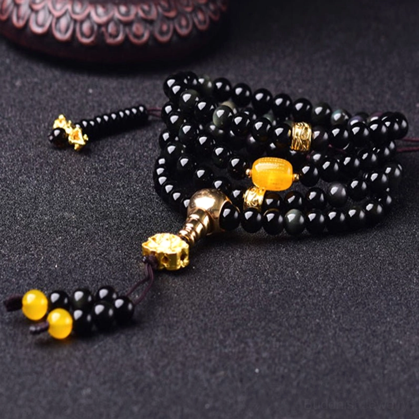 Stacked black obsidian mala bracelet with amber central bead and gold fasteners photographed on dark background