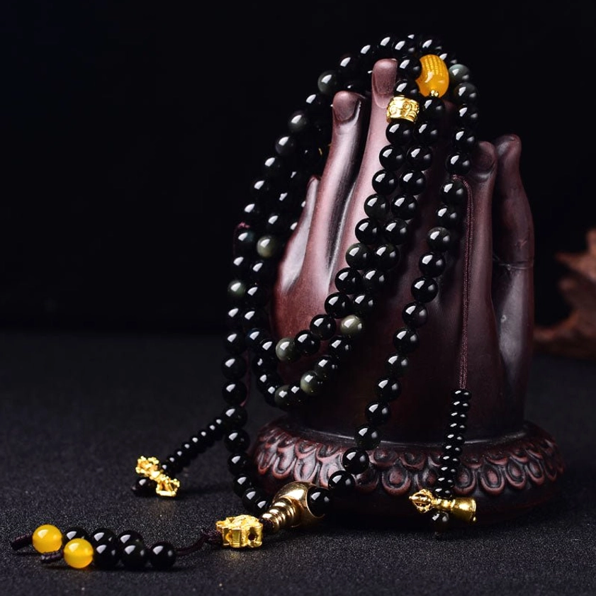 Buddhist mala bracelet with black obsidian beads displayed on wooden Buddha hand stand showing polished beads and gold details