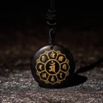 Black Obsidian Om Mani Padme Hum Buddhist necklace pendant with gold Sanskrit engraving and black braided cord, front close-up view