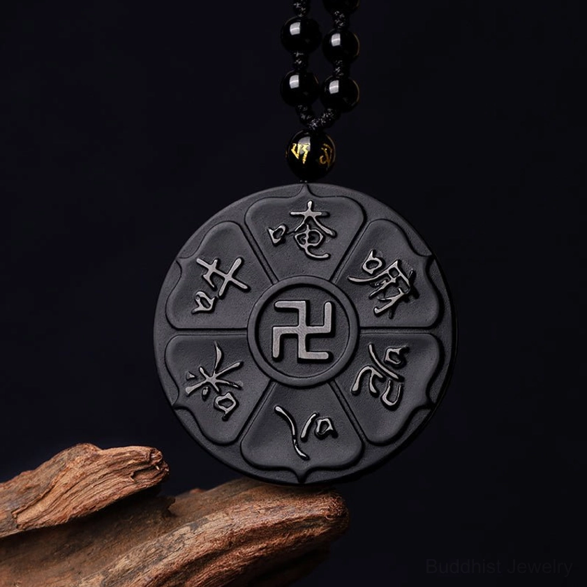Black obsidian Buddhist pendant with Om Mani Padme Hum and swastika carved symbols flat lay view