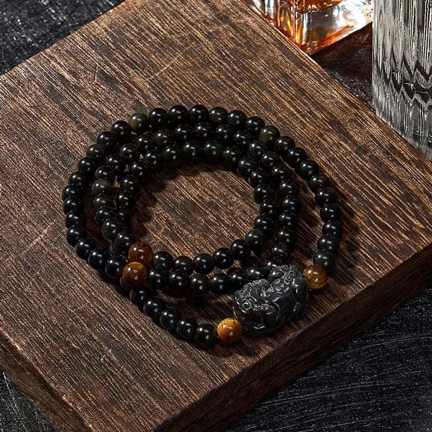 Hand-carved black Pixiu obsidian bracelet flat lay on dark wood background with iridescent bead accents
