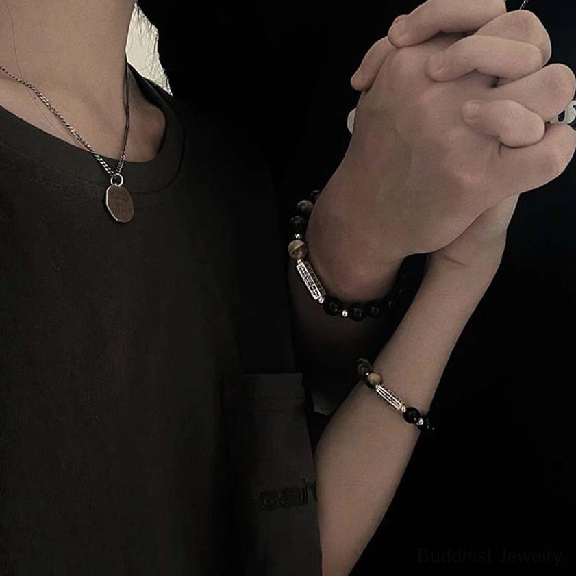 Woman wearing obsidian tiger eye beaded bracelets on both wrists with pendant necklace, close-up hands clasped together casual styling