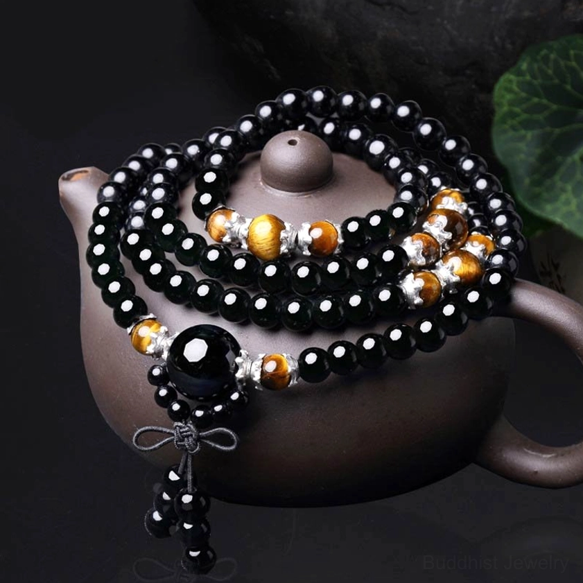 Black Obsidian and Tiger Eye 108 bead Buddhist prayer mala bracelet with silver spacers and tassel pendant displayed on dark surface