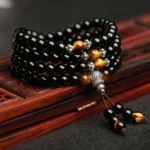 Black obsidian tiger eye Buddhist mala bracelet close-up with silver guru bead, displayed on red wooden tray