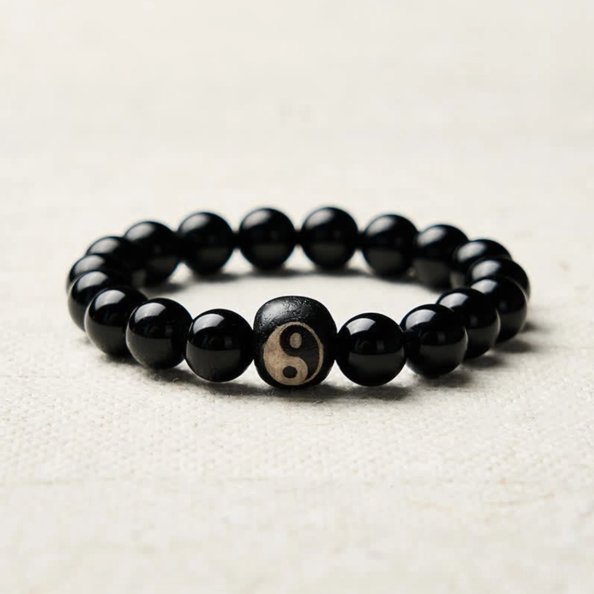 Black obsidian yin yang beaded bracelet polished round beads light beige background flat lay