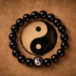 Black obsidian yin yang beaded bracelet with engraved centerpiece on brown leather background top view
