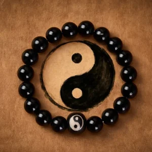 Black obsidian yin yang beaded bracelet with engraved centerpiece on brown leather background top view